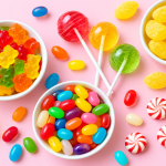 Colorful dialysis-friendly candies, including gummy bears, clear lollipops, lemon drops, jelly beans, and peppermint sweets arranged on a soft pastel pink background.